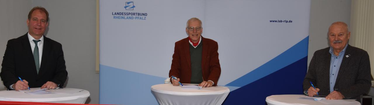 Randolf Stich Innenministerium Joachim Schulte QueerNet RLP und Wolfgang Bärnwick Landessportbund Rheinland-Pfalz an Stehtischen und unterschreiben den Kooperationsvertrag.