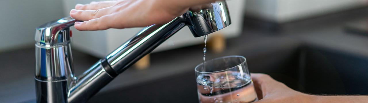 Hand, die ein Glas am Wasserhahn füllt