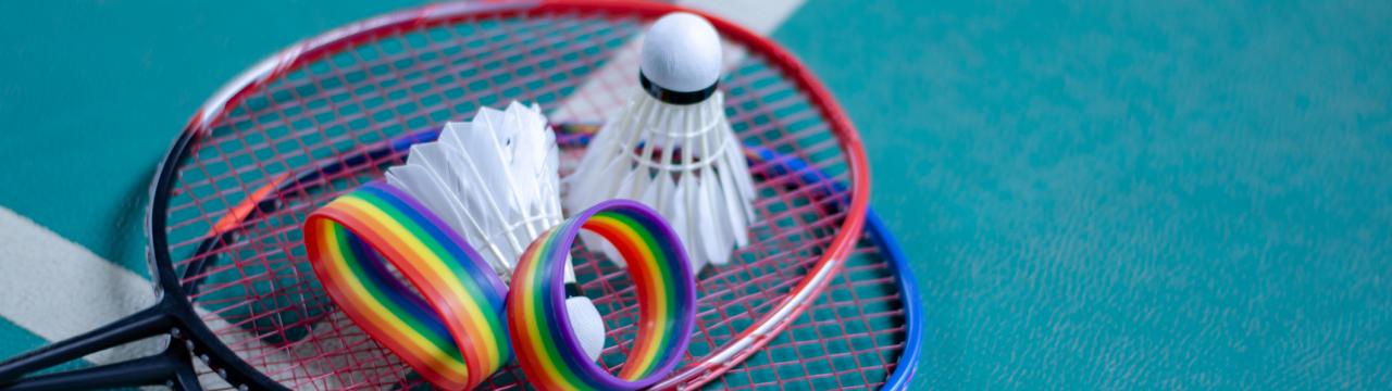 Regenbogenfarbene Armbänder, Federball und Schläger auf dem Boden eines Hallenplatzes.