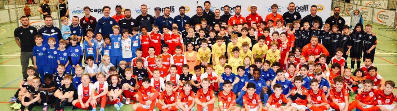 Gruppenfoto mit Beteiligten des Cage Soccer Turniers 2026. Zu sehen sind Spieler*innen, Trainer*innen und Helfer*innen.