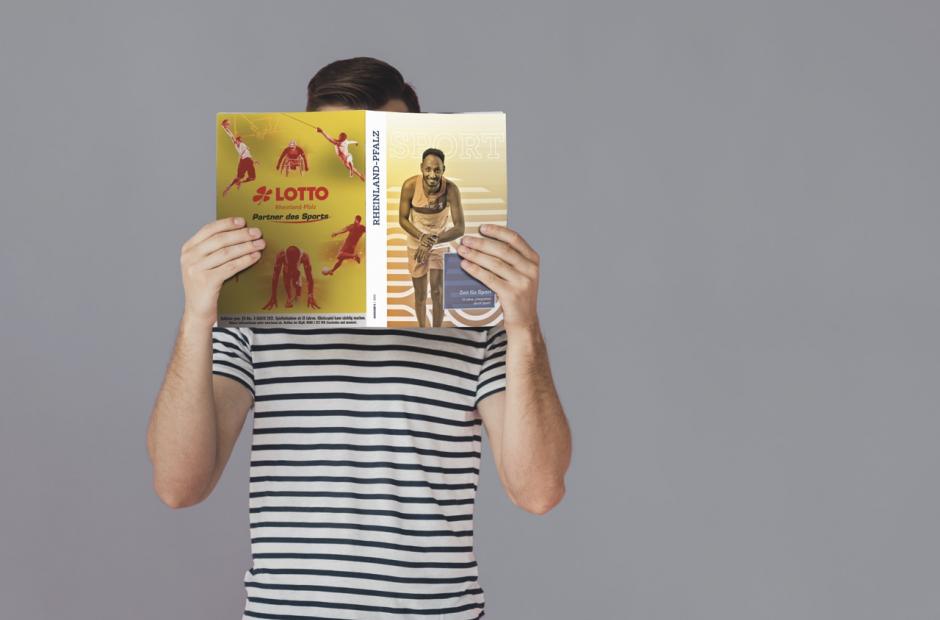 Person, die eine Ausgabe der Sport RLP vor dem Gesicht in den Händen hält