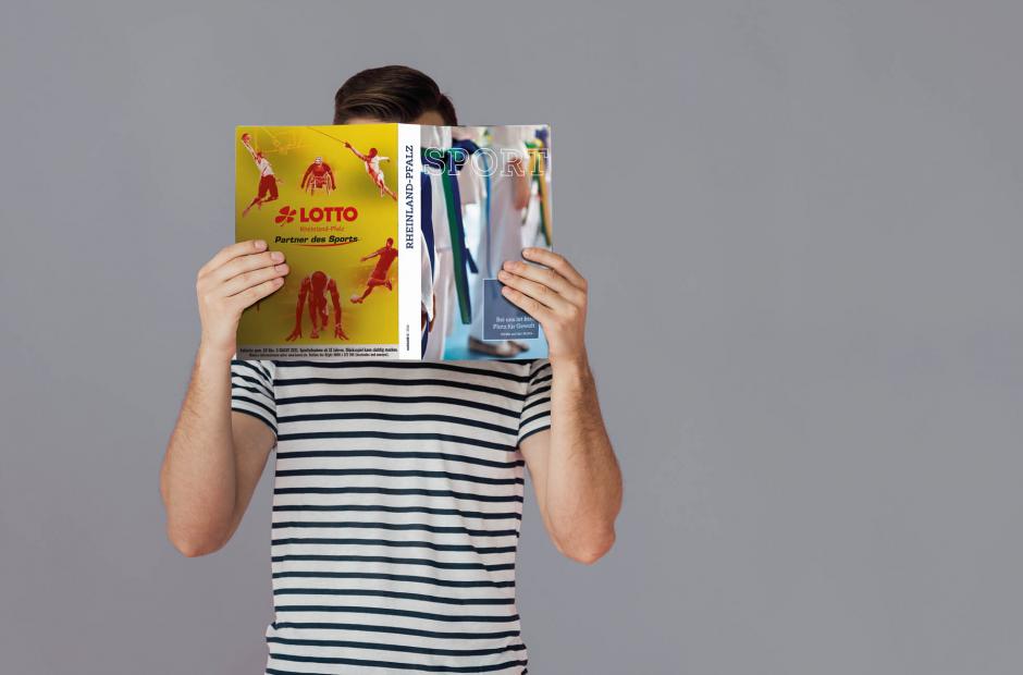 Person, die eine Ausgabe der Sport RLP vor dem Gesicht in den Händen hält