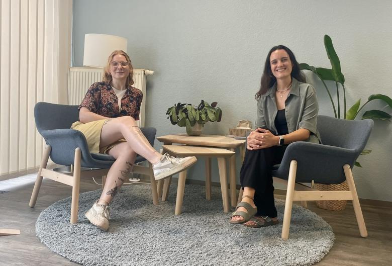 Zwei Frauen sitzen auf Stühlen und schauen in die Kamera