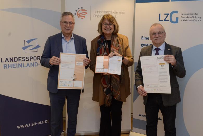 Drei Personen stehen nebeneinander und halten Dokumente in die Kamera