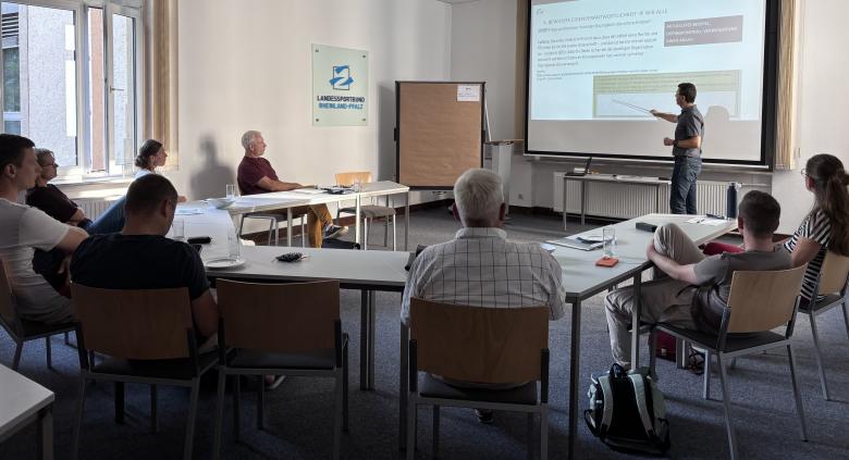 Personen an Tischen in Versammlungsraum
