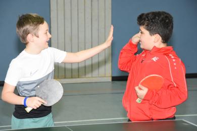 Zwei Jungen klatschen sich an Tischtennisplatte freundschaftlich ab