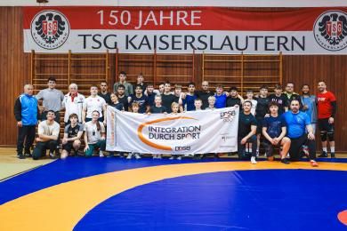 Tag der offenen Tür der "Offenen Ringergruppe Kaiserslautern": Gruppenfoto aller Teilnehmer*innen mit einem Banner von "Integration durch Sport".