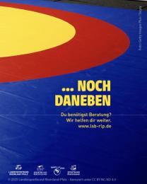 "...noch daneben" auf Foto einer blau-rot-gelben Ringermatte