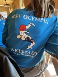 Das Foto zeigt den Rücken der freiwillig Engagierten Jasmin Rimmer. Sie trägt eine Trainingsjacke, die auf dem Rücken mit dem Namen des Vereins "RSV Olympia Neustadt" beschriftet und auf welcher zwei Ringer*innen in Aktion abgebildet sind.