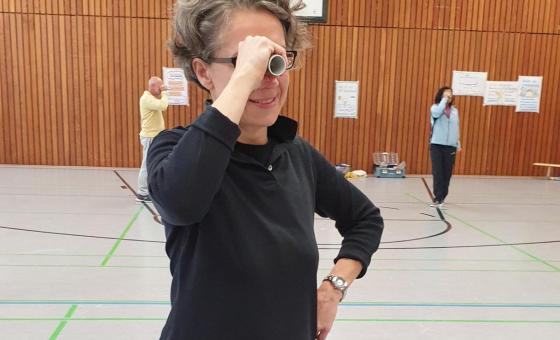 Frau steht auf einem Bein und schaut durch ein "Fernglas"