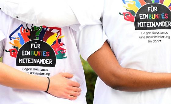 Junge Sportler (von hinten) stehen umarmend nebeneinander 