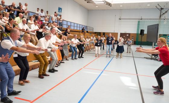 Menschen in einer Turnhalle machen Kniebeugen.