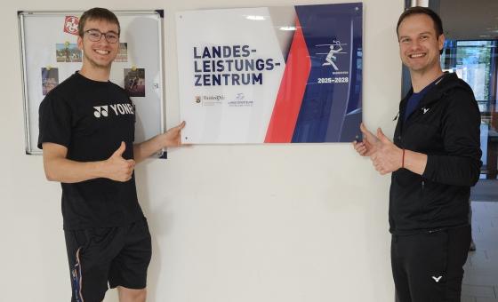 Zwei Männer vor Schild in Sporthalle