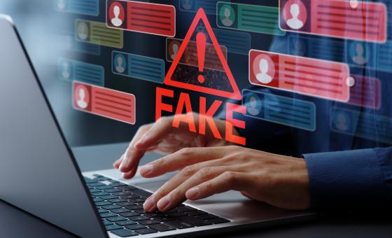 Hände, die auf einer Laptoptastatatur tippen. Schriftzug in Rot: Fake