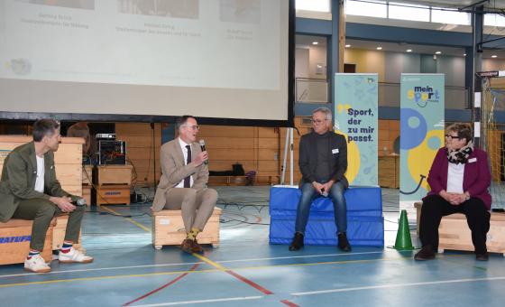 Personen sitzend in Sporthalle